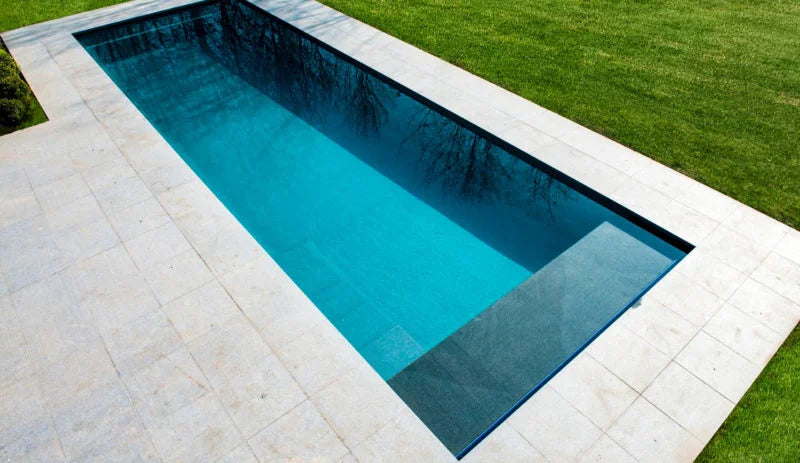 Modern rektangulär pool med turkost vatten och beige stenplattor i effektivt underhållsschema.