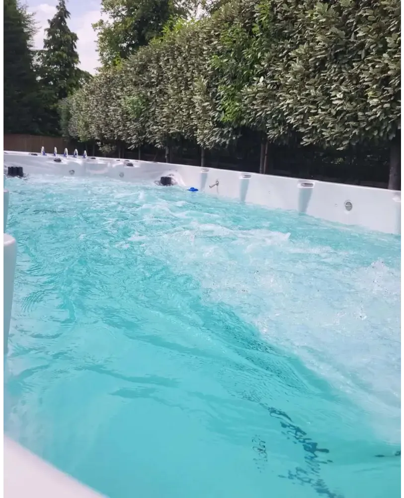 Vit PassionSpa Spirit Deep Swim Spa med turkost vatten och jetstrålar omgiven av gröna träd