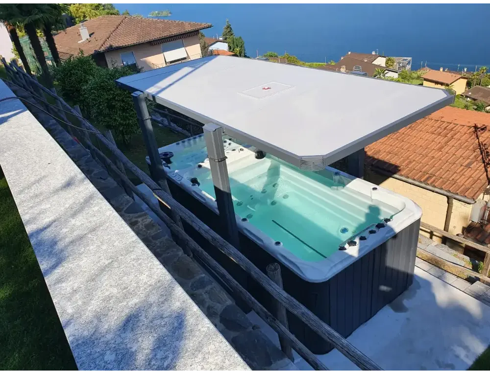 Grå PassionSpa Spirit Swim Spa med vit lock och svarta jetstrålar på stenaltan vid havet