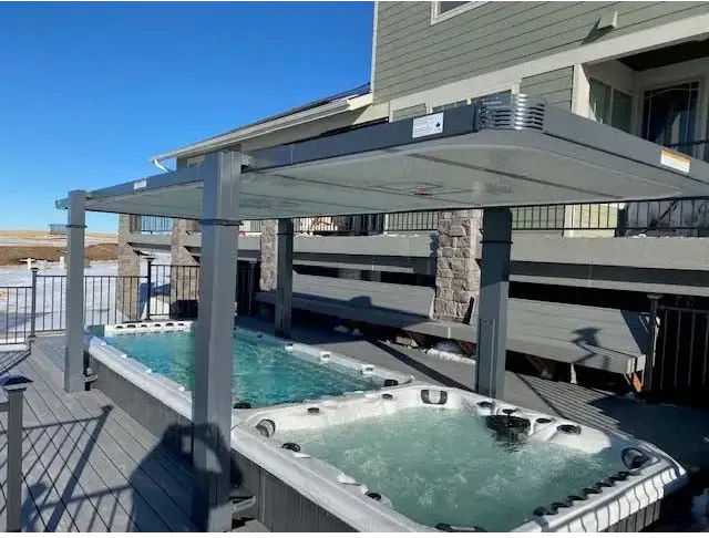 Grå metallpatioöverdrag med transparenta paneler över två PassionSpa Vitality Deep Swim Spa-hottubs